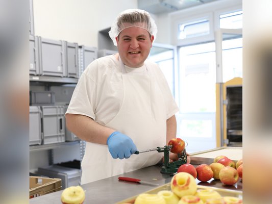 Ein Mitarbeiter der arwo Stiftung bereitet in der Lebensmittelproduktion frische Früchte zu.